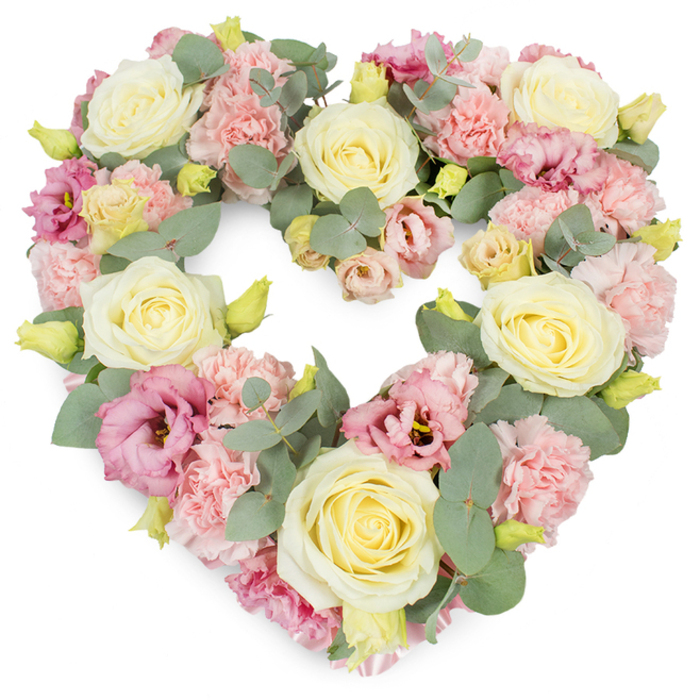 A lush, heart-shaped wreath of sympathy flowers is presented against a clean white backdrop, allowing every detail of the arrangement to stand out with quiet clarity. The entire heart form is densely packed, giving it a rich, substantial presence that speaks of deep care and thoughtfulness. At the core of the design are large, creamy ivory and soft lemon-yellow roses, their tightly layered petals opening into generous blooms that radiate a sense of purity and affection. These roses are carefully spaced to create rhythm and balance across the heart, as an experienced Hatch End florist might do when preparing flowers for a local memorial service. Between the roses, ruffled pastel pink carnations crowd together, their feathered edges and gentle blush tones softening the whole outline into something that feels like a tender embrace. Threaded throughout are lisianthus blossoms in shades of rose-pink and mauve, some more open, others still unfurling, their slightly fluted petals adding depth and a romantic, almost wistful character. Sprays of silvery eucalyptus weave through the flowers, the rounded leaves resting lightly on the petals and adding a cool, calming green that contrasts beautifully with the warm pastels. Tiny yellow-green buds punctuate the composition, offering hints of new growth and the quiet promise that memories will continue to bloom. The white background ensures the heart shape is clearly defined, making it easy to imagine this tribute resting by the front of a chapel in Hatch End, or delivered to a family home near Uxbridge Road as a heartfelt gesture of condolence. The overall mood is one of gentle remembrance, comfort, and enduring love for someone greatly missed.