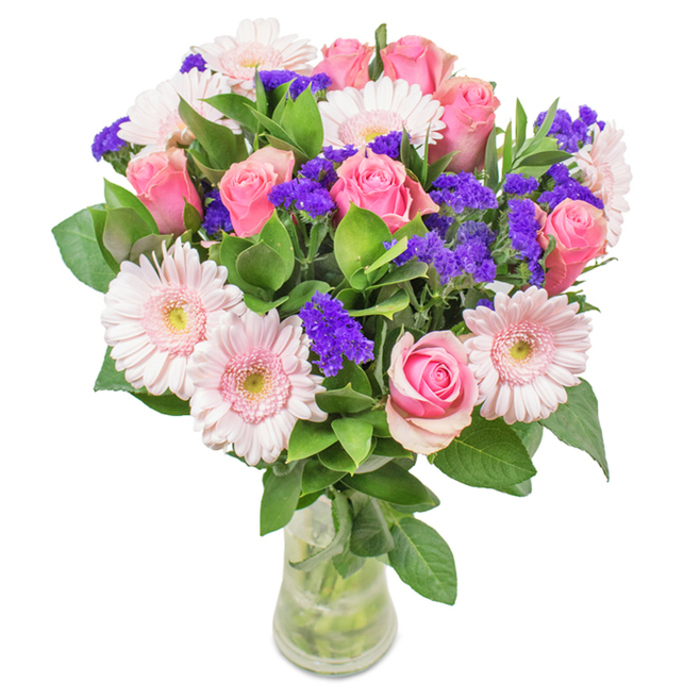 A beautifully composed bouquet takes centre stage, thoughtfully arranged by a Hatch End florist to highlight the serene palette of its surroundings. Approximately seven to nine pink roses-some tightly furled, some gently opened-display their classic spirals in a clear glass vase. They are complemented by five to seven pale pink gerbera daisies, easily distinguished by their generous round faces and radiating petals, with centres hinting at the delicate whites found in tranquil local gardens. Vivid clusters of purple statice are nestled among the larger blooms, providing striking contrast and depth, much like the seasonal contrast seen in Hatch End's tree-lined avenues. Deep green foliage weaves through the arrangement, offering a velvety texture and natural volume, enhancing the bouquet's lush, abundant feel. The visible stems and fresh water within the transparent vase reinforce the sense of immediacy and offering, as though hand-delivered from a local flower market. This elegant arrangement of pink roses, gerbera daisies, and purple filler flowers is suited for occasions such as birthdays, anniversaries, Mother's Day, or as an expressive centrepiece for a modern home or Hatch End office. The bouquet's vibrant colours, coupled with its fresh scent and refined presentation, convey lasting affection, optimism, and a touch of the artistry that flourishes throughout the local community.